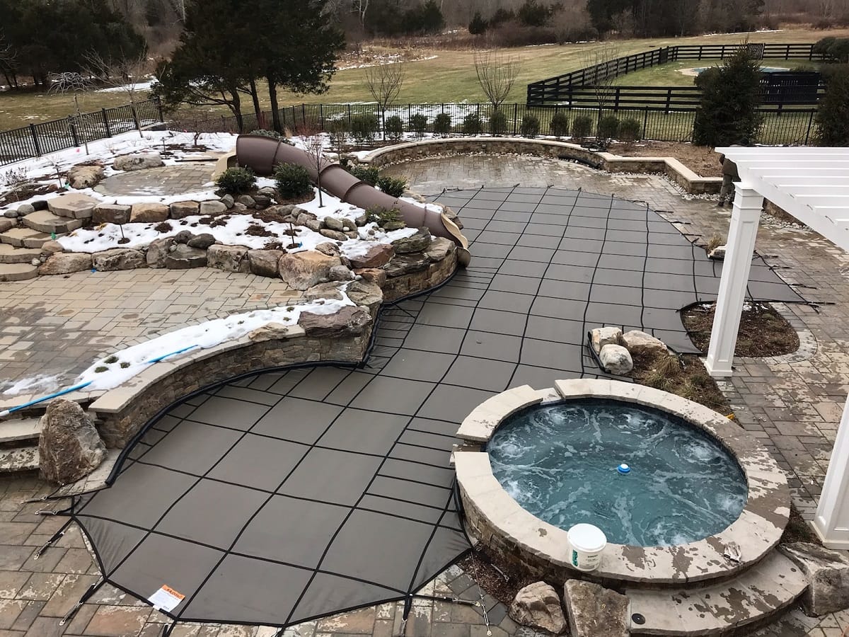 Freeform pool with rock waterfall and round spa under a custom mesh safety cover