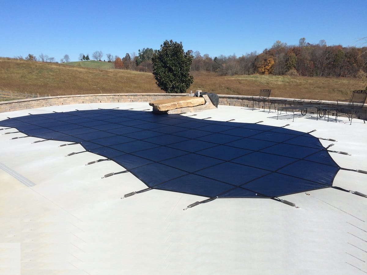 Large pool under a dark blue safety cover on a hillside property