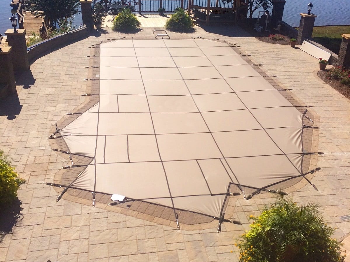 Tan safety cover on a pool surrounded by brick pavers